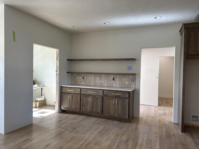 kitchen with open shelves, light wood-style floors, light countertops, dark brown cabinets, and a textured ceiling
