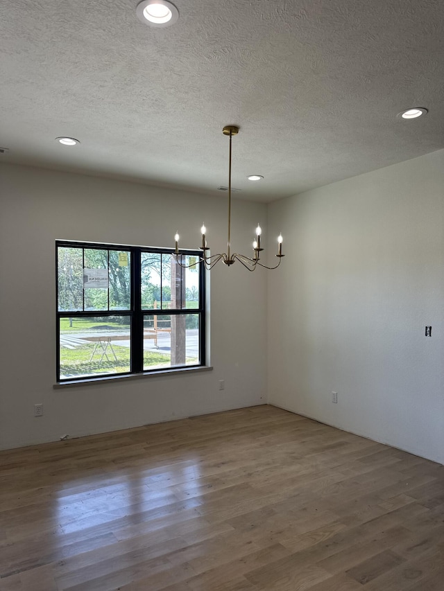 spare room featuring a chandelier, a textured ceiling, wood finished floors, and recessed lighting