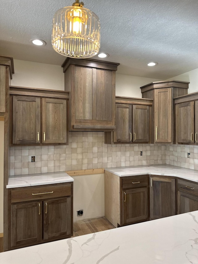 kitchen with decorative backsplash, a textured ceiling, wood finished floors, light stone counters, and recessed lighting