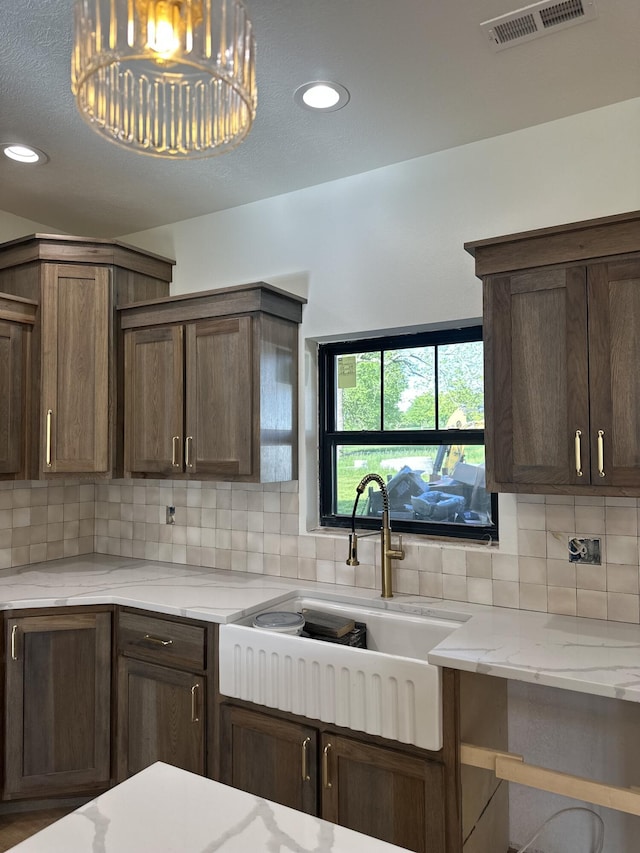 kitchen with a sink, backsplash, light stone countertops, recessed lighting, and dark brown cabinets