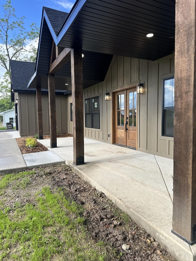 entrance to property featuring board and batten siding, french doors, roof with shingles, and a patio