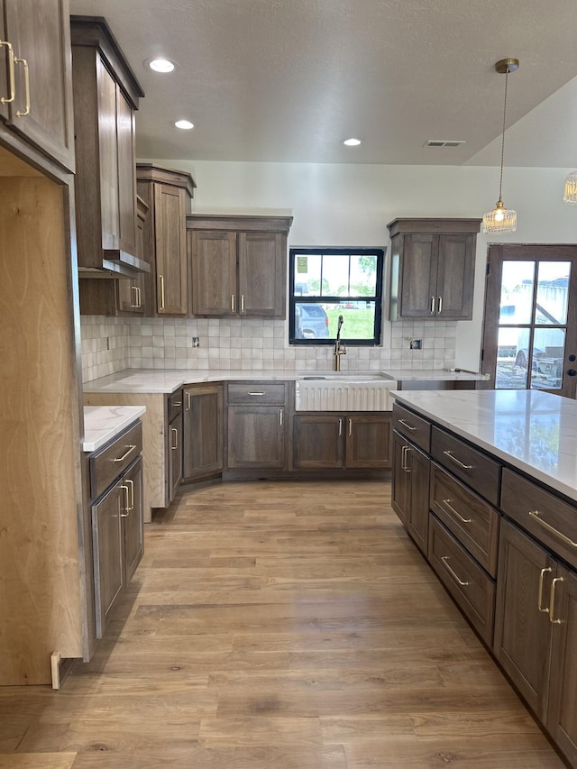kitchen with a sink, plenty of natural light, decorative backsplash, light wood finished floors, and recessed lighting