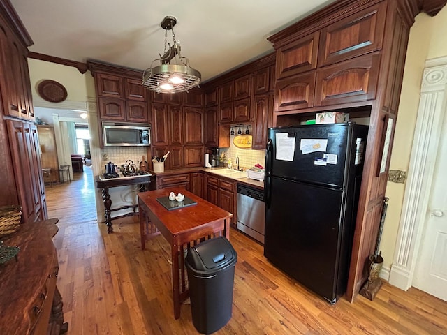 kitchen with stainless steel appliances, decorative backsplash, a sink, and light wood finished floors