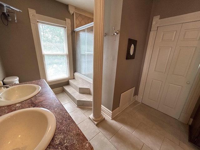 bathroom with a shower with door, baseboards, tile patterned flooring, and double vanity