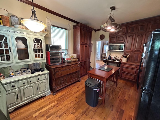 kitchen featuring freestanding refrigerator, stainless steel microwave, light wood-style floors, ornamental molding, and pendant lighting