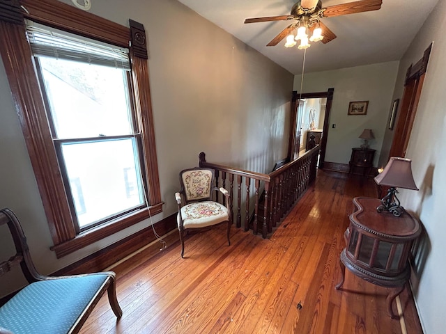 sitting room with wood-type flooring, a ceiling fan, an upstairs landing, and baseboards