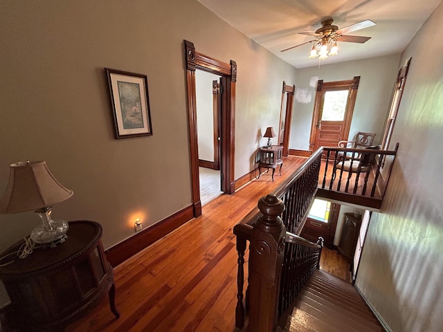 corridor with an upstairs landing, hardwood / wood-style floors, and baseboards