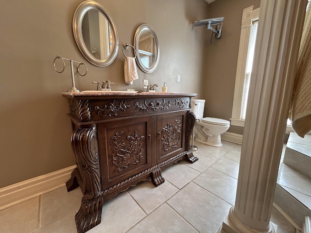 bathroom with toilet, tile patterned floors, baseboards, decorative columns, and double vanity