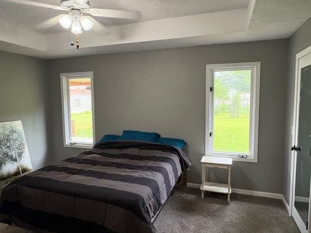 carpeted bedroom featuring baseboards, a raised ceiling, and ceiling fan