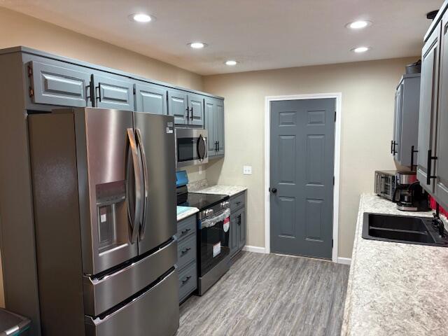 kitchen with appliances with stainless steel finishes, light countertops, light wood-style floors, recessed lighting, and a sink