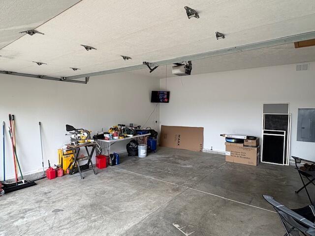 garage featuring electric panel, a garage door opener, and a workshop area