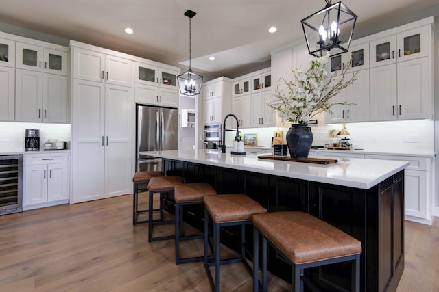 kitchen featuring wine cooler, a chandelier, decorative backsplash, appliances with stainless steel finishes, and a center island with sink