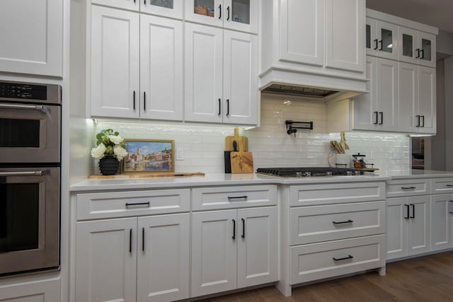 kitchen featuring appliances with stainless steel finishes, white cabinets, light countertops, glass insert cabinets, and tasteful backsplash