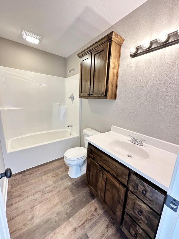 1712 S Jackson St, El Dorado Springs, MO 64744 - full bath featuring wood finished floors, shower / washtub combination, vanity, and toilet
