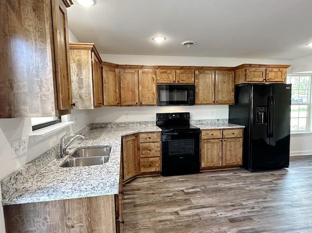 1712 S Jackson St, El Dorado Springs, MO 64744 - kitchen with black appliances, a sink, brown cabinetry, wood finished floors, and light stone counters