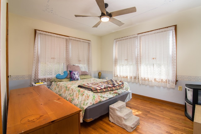 bedroom featuring multiple windows, wood finished floors, ceiling fan, and baseboards