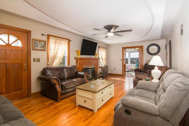 living area featuring ceiling fan, light wood-style floors, a fireplace, and baseboards