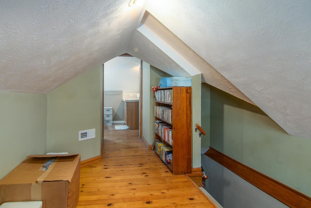 bonus room with a textured ceiling, light wood finished floors, vaulted ceiling, and baseboards