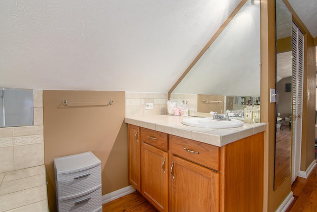 bathroom with vanity, baseboards, wood finished floors, backsplash, and lofted ceiling