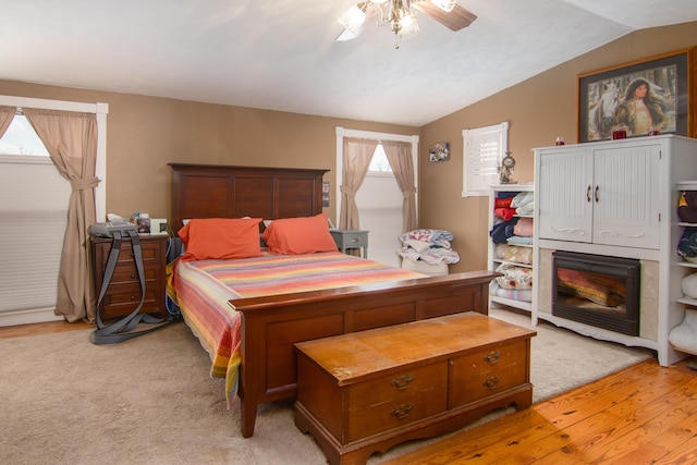 bedroom featuring vaulted ceiling, multiple windows, a fireplace, and ceiling fan