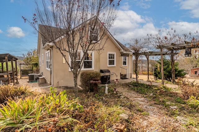 view of side of property featuring central AC, a pergola, stucco siding, and fence
