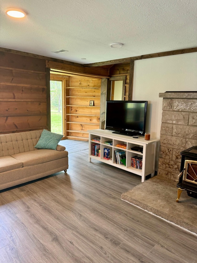 living area with a wood stove, a textured ceiling, wood finished floors, and rustic walls