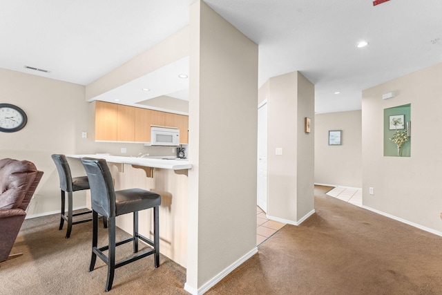 351 S Wildwood Dr Unit 3-2, Branson, MO 65616 - kitchen featuring white microwave, light carpet, a kitchen breakfast bar, light countertops, and light brown cabinetry