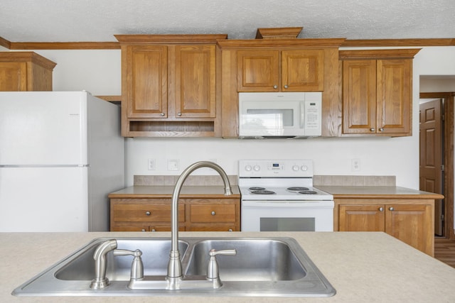 kitchen with white appliances, a sink, brown cabinets, light countertops, and a textured ceiling