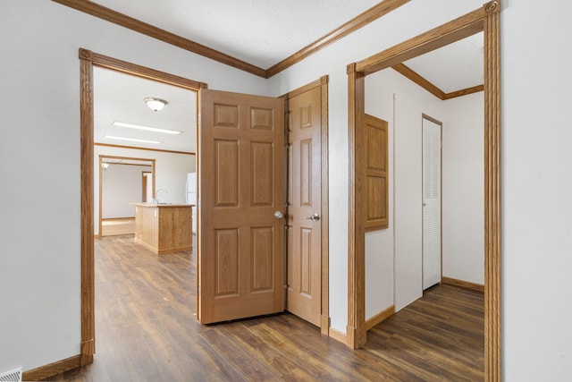 hall with dark wood-style floors, ornamental molding, baseboards, and a sink