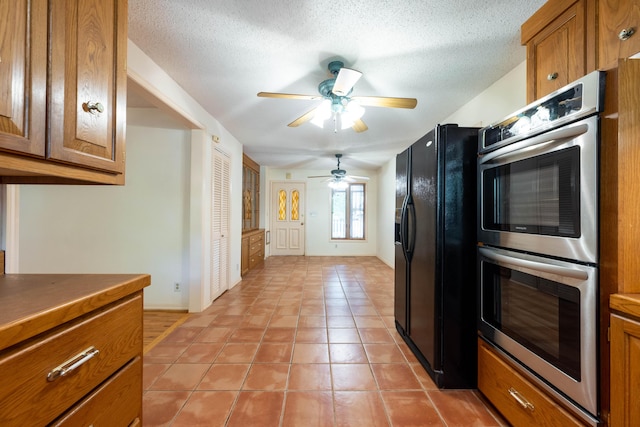 kitchen featuring black fridge, double oven, brown cabinetry, ceiling fan, and baseboards