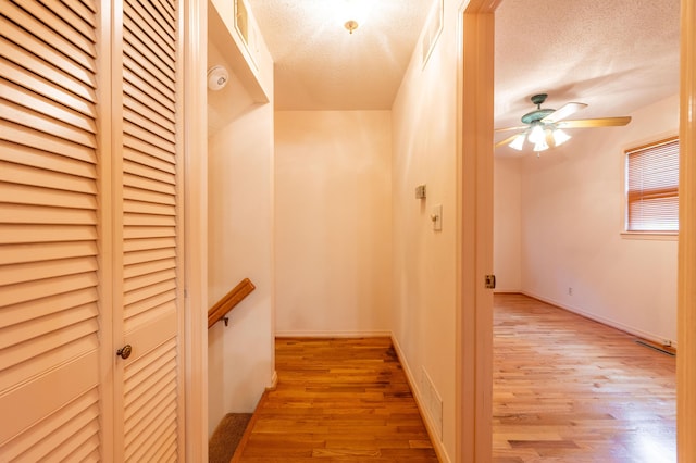 corridor featuring light wood-style floors, a textured ceiling, and an upstairs landing