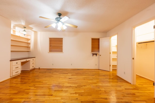 unfurnished bedroom featuring light wood-style floors, a textured ceiling, baseboards, a ceiling fan, and a spacious closet