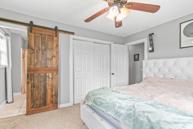 bedroom with a barn door, a closet, carpet, a ceiling fan, and baseboards