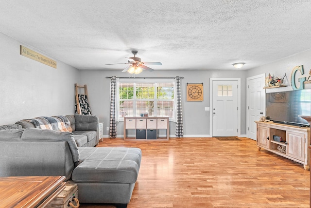 living room with ceiling fan, light wood-style floors, a textured ceiling, and baseboards