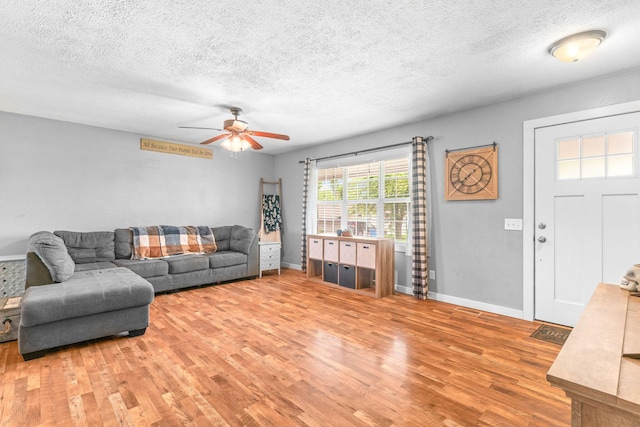 living room featuring light wood-style floors, a ceiling fan, a textured ceiling, and baseboards
