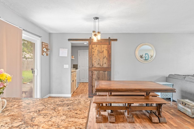 dining space featuring a barn door, light wood-style floors, and a textured ceiling