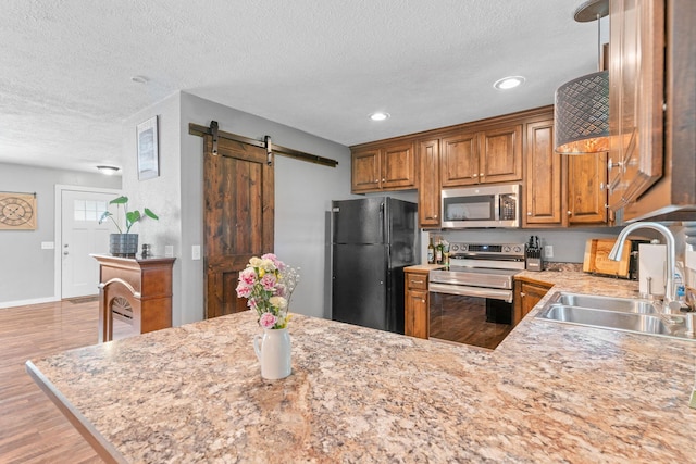 kitchen with stainless steel appliances, a sink, a barn door, wood finished floors, and a textured ceiling