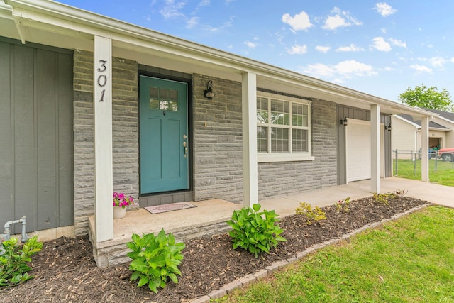 doorway to property featuring an attached garage, concrete driveway, and covered porch