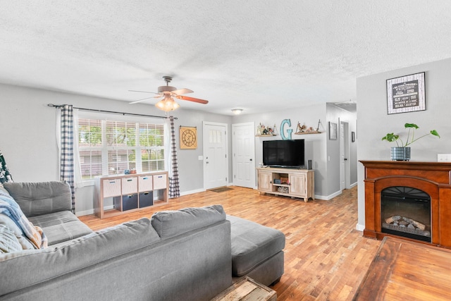 living room with light wood-style floors, ceiling fan, a textured ceiling, baseboards, and a fireplace