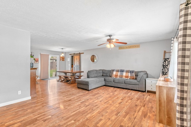living area with light wood-style flooring, a ceiling fan, a textured ceiling, and baseboards