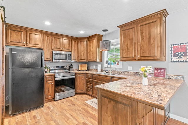 kitchen with stainless steel appliances, a sink, brown cabinetry, light wood-style flooring, and recessed lighting