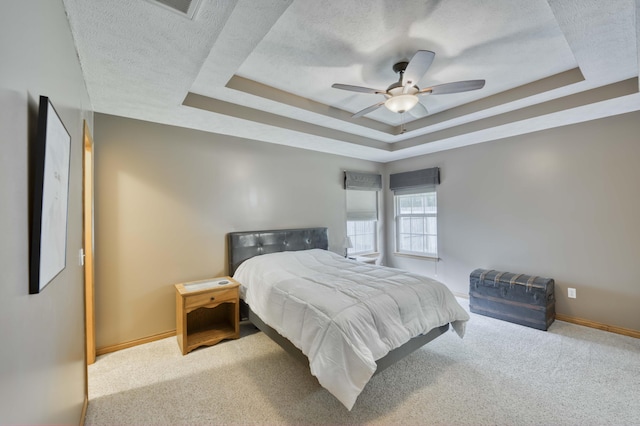 carpeted bedroom with a tray ceiling, a textured ceiling, baseboards, and ceiling fan