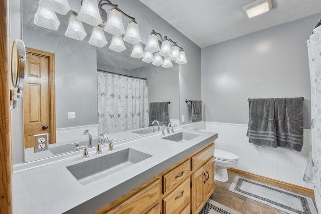 bathroom with a wainscoted wall, toilet, double vanity, and curtained shower