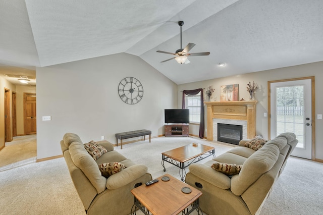 living area with light carpet, lofted ceiling, a ceiling fan, a glass covered fireplace, and plenty of natural light