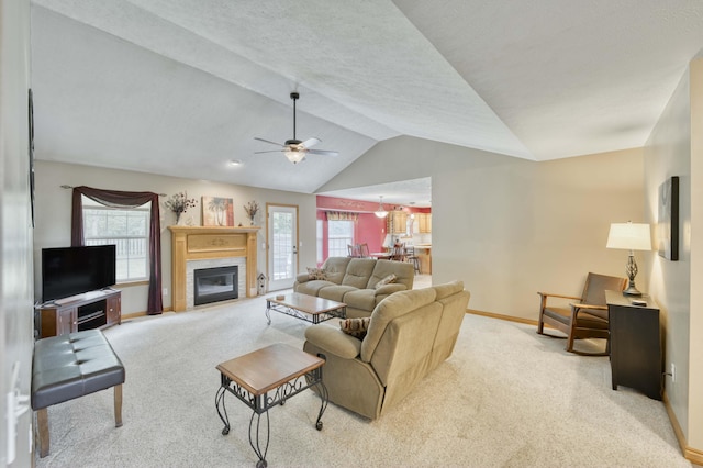 carpeted living room featuring vaulted ceiling, baseboards, ceiling fan, healthy amount of natural light, and a glass covered fireplace