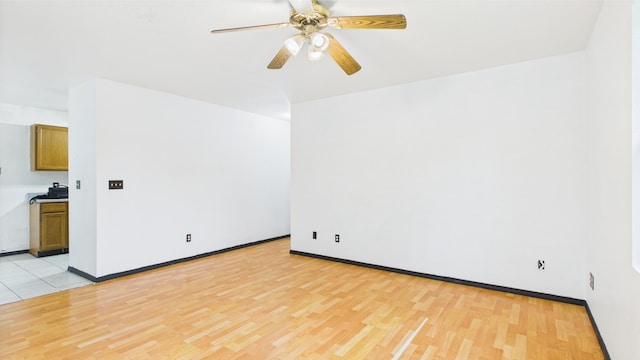 empty room with light wood finished floors, a ceiling fan, and baseboards