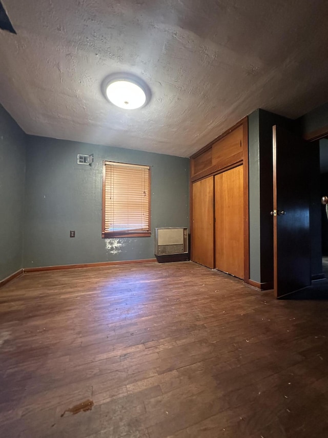 unfurnished bedroom with wood finished floors, a textured ceiling, baseboards, and a closet