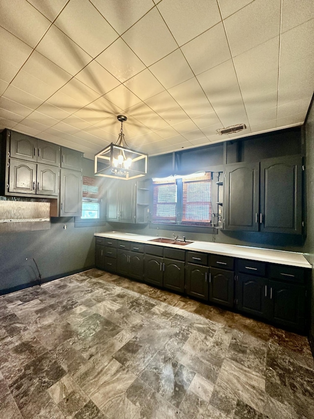 kitchen with a sink, a chandelier, decorative light fixtures, light countertops, and stone finish flooring