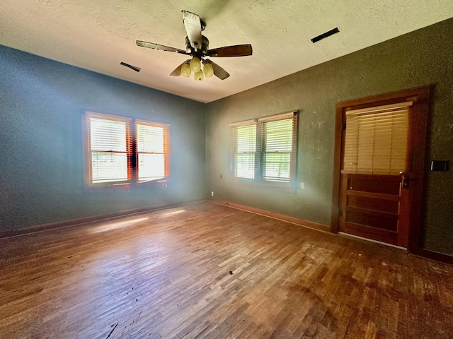 spare room featuring hardwood / wood-style flooring, a textured wall, a ceiling fan, a textured ceiling, and baseboards