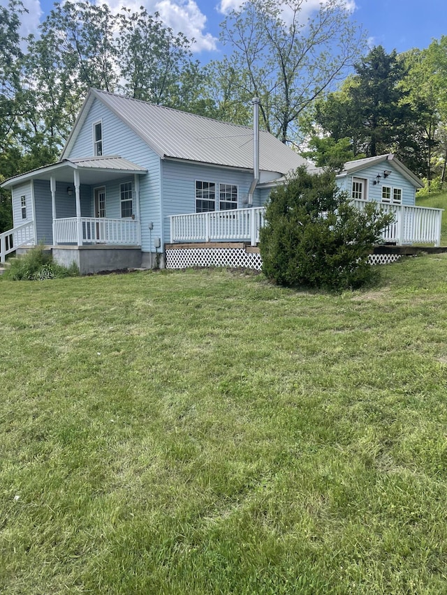 rear view of property featuring a lawn, metal roof, a deck, and covered porch